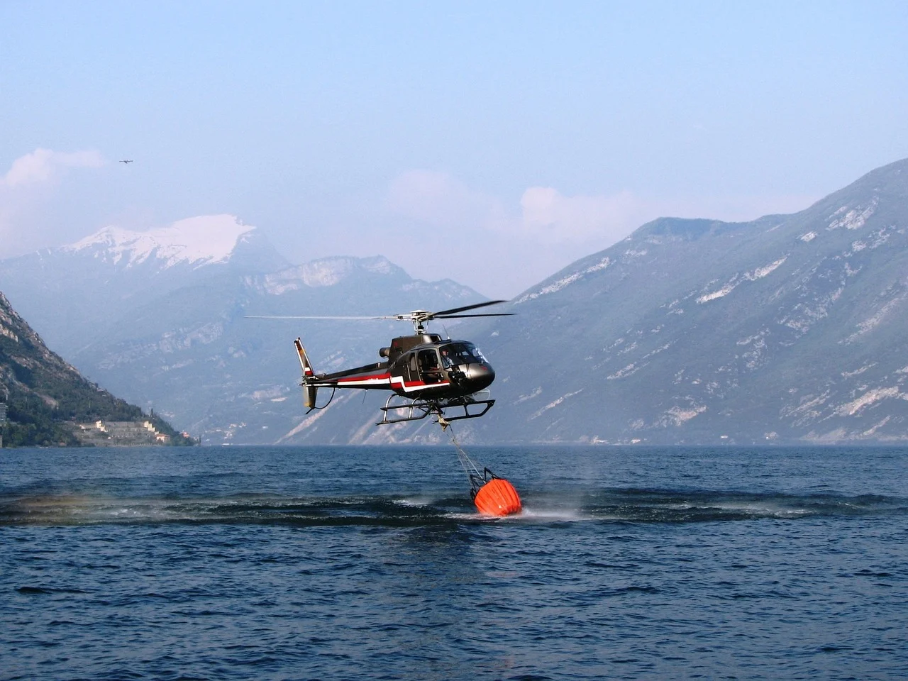 Helicóptero recogiendo agua de un lago con un helibalde para combatir incendios forestales