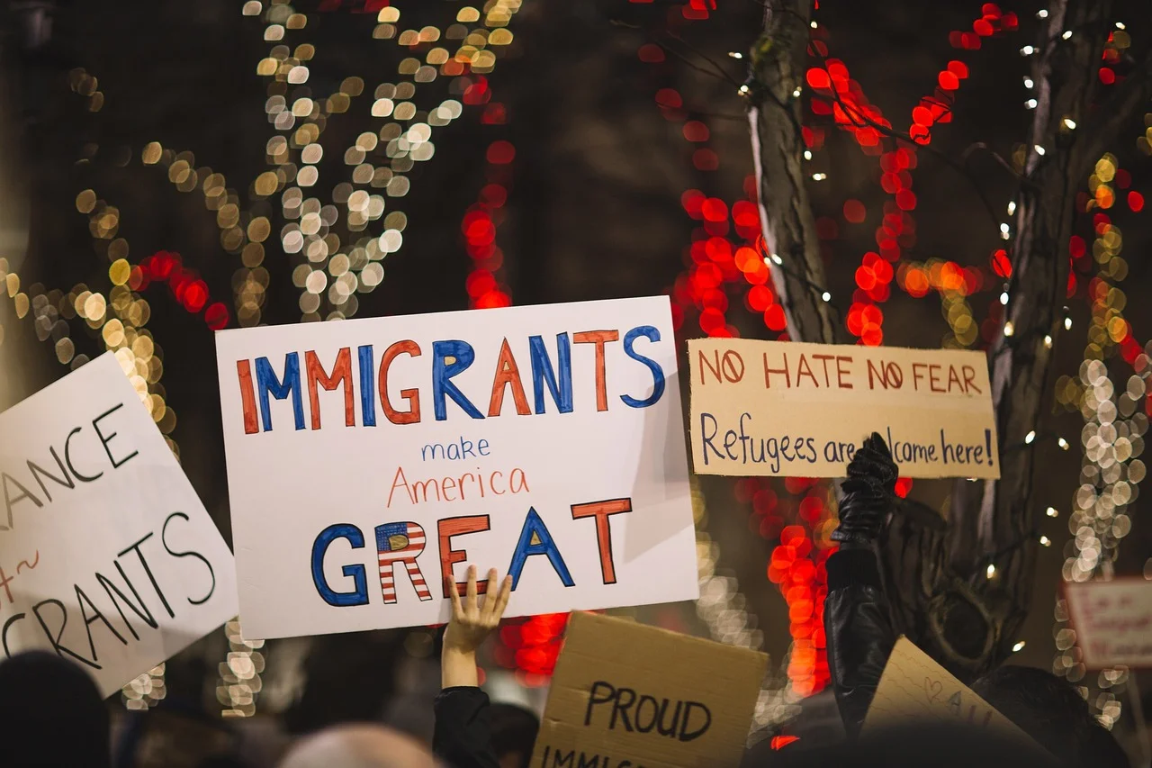 Manifestación con pancartas en apoyo a inmigrantes y refugiados que dicen Los inmigrantes hacen a Estados Unidos grande y Sin odio sin miedo los refugiados son bienvenidos aquí