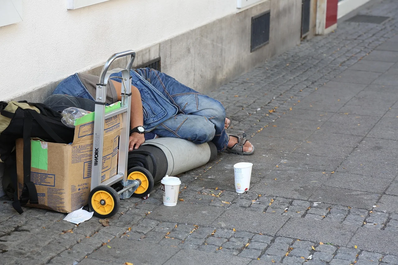 Persona sin hogar durmiendo en la calle junto a una caja y vasos de cartón, símbolo de la pobreza urbana.