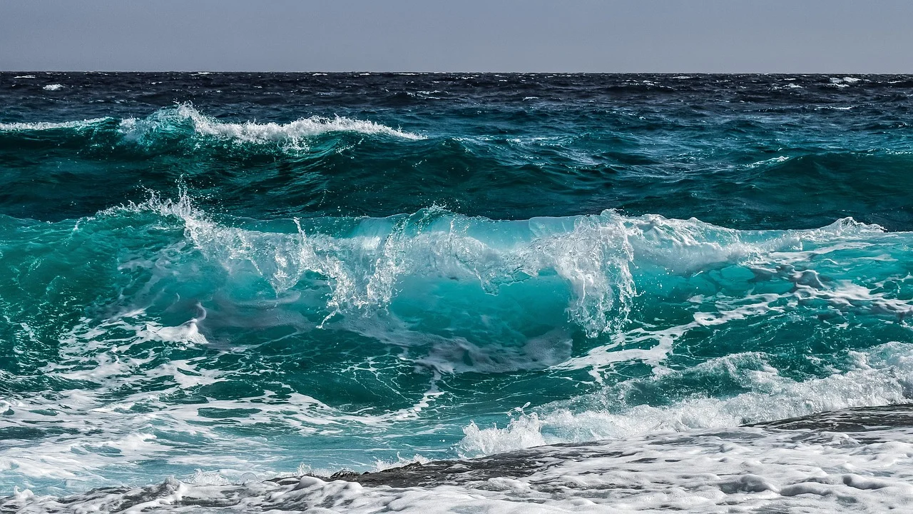 Ola rompiendo en la playa con espuma blanca y agua turquesa en movimiento, mostrando la fuerza del mar y la belleza del océano