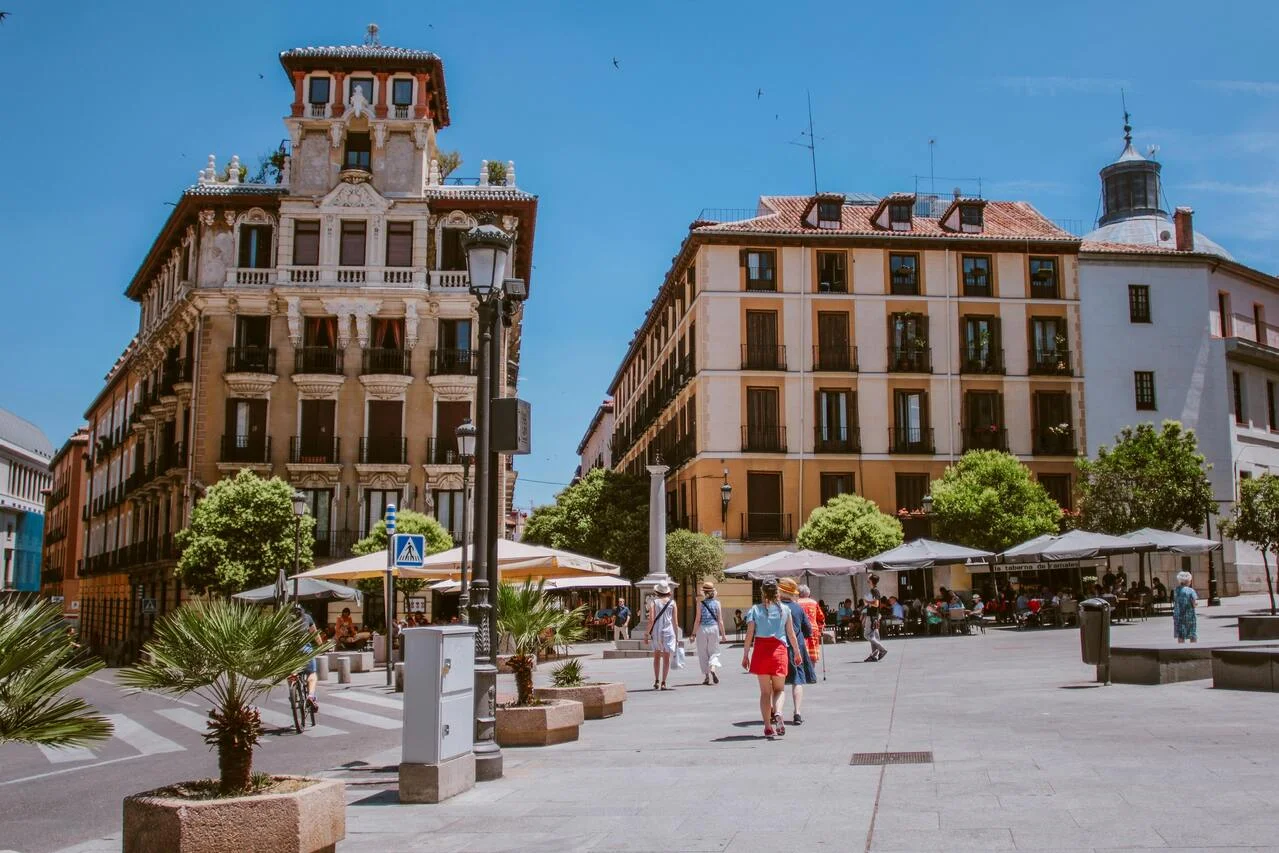 Plaza urbana en Madrid con edificios históricos, terrazas de cafeterías y turistas paseando en un día soleado