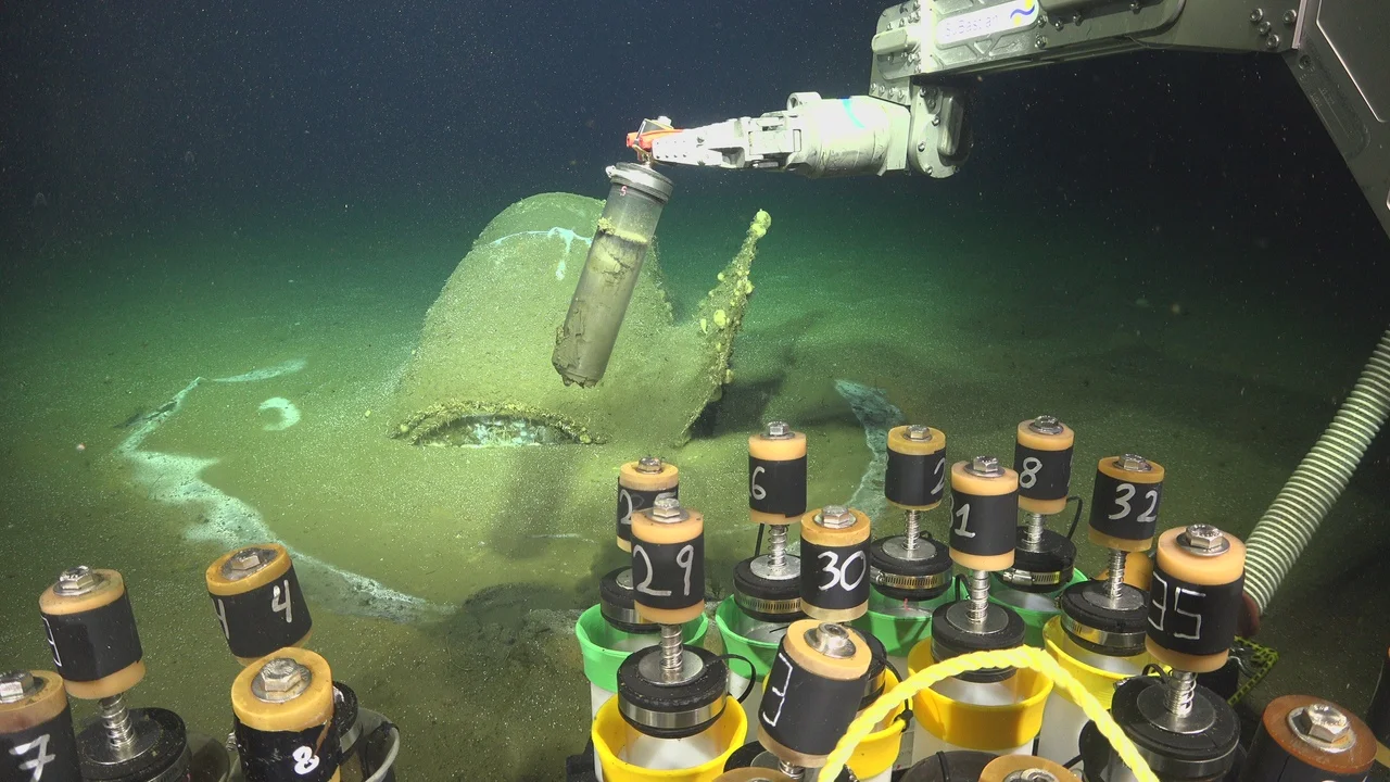 ROV utilizando su brazo manipulador para tomar muestras cerca de un barril en el fondo marino