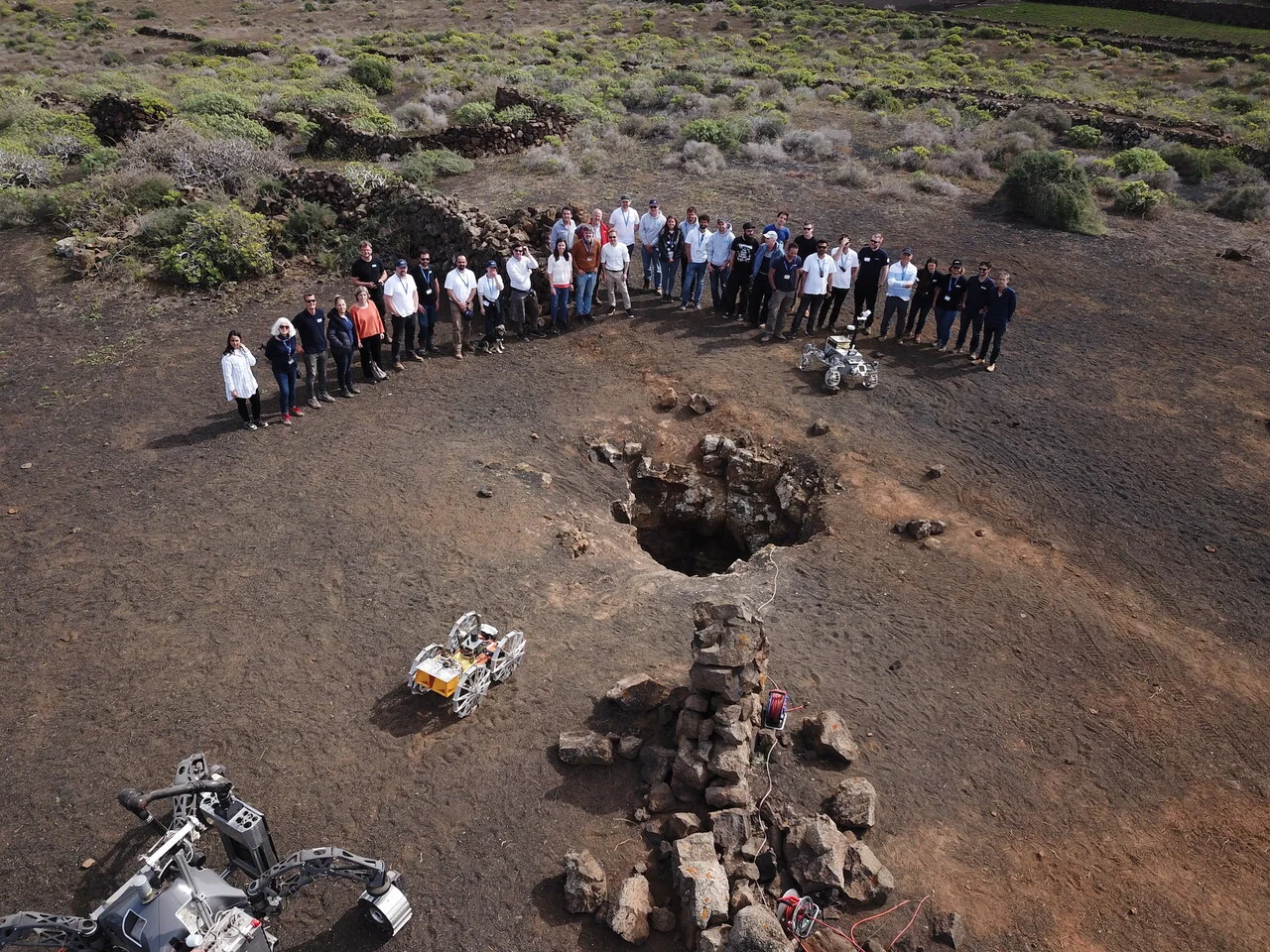 Equipo de investigadores del proyecto CoRobX y tres robots espaciales reunidos junto a la entrada de un tubo volcánico en Lanzarote
