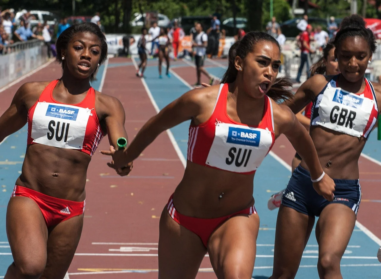 Atletas compiten en una carrera de relevos femeninos en pista de atletismo durante el momento del pase del testigo