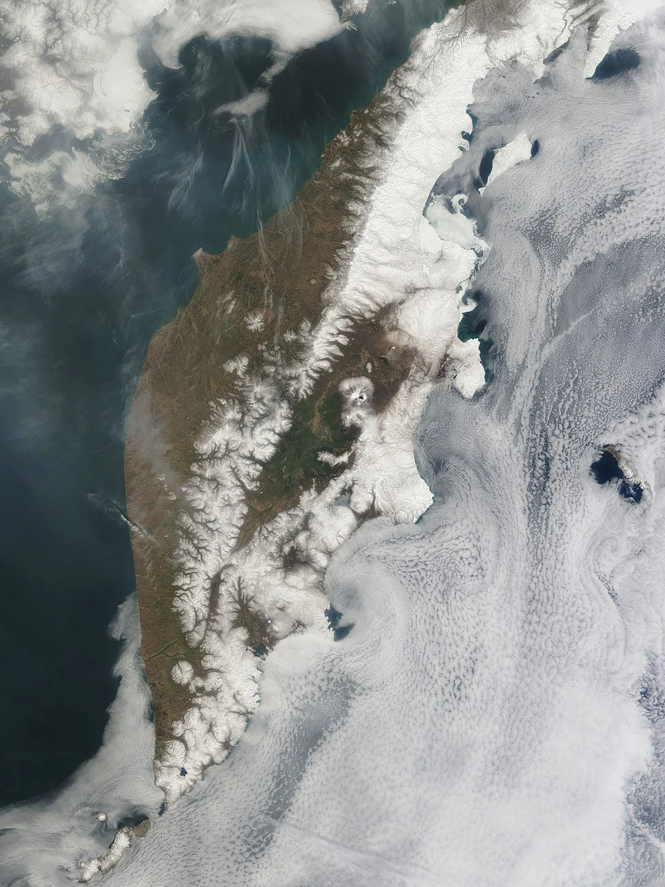 Imagen satelital de la península de Kamchatka cubierta parcialmente por nieve y nubes, captada por la NASA