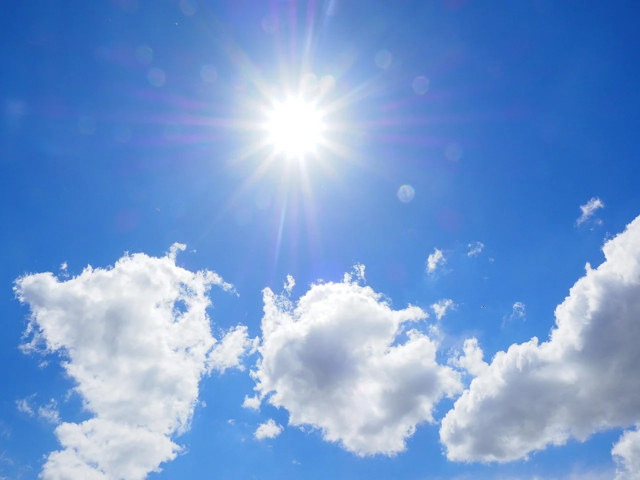 Cielo azul con sol brillante y nubes blancas, representando calor extremo y altas temperaturas durante el verano