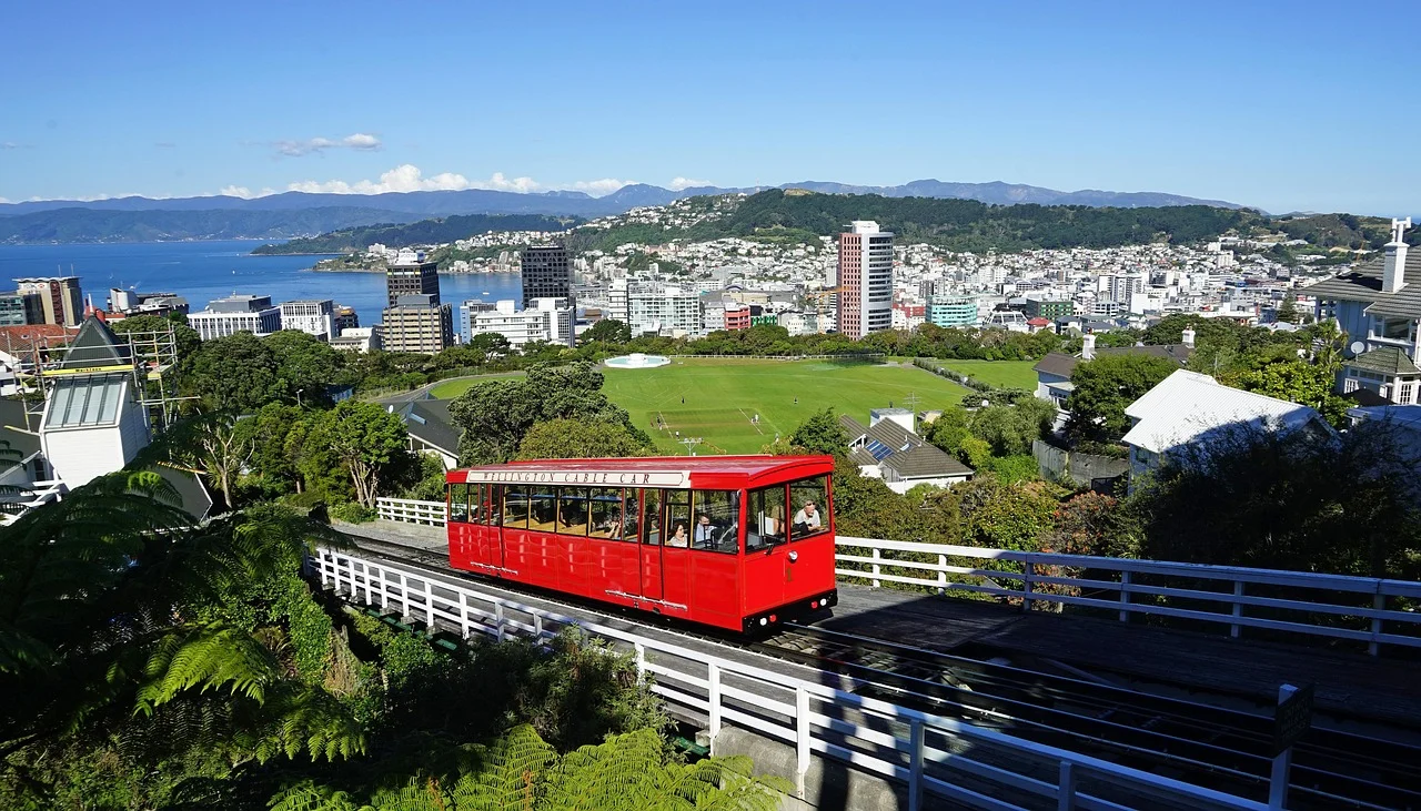 Tranvía rojo en Wellington, Nueva Zelanda, con vista panorámica de la ciudad, colinas y el mar de fondo