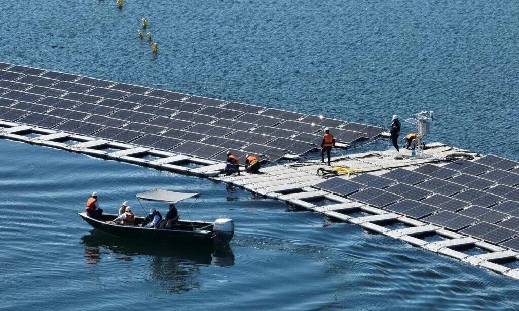 Trabajadores instalando paneles solares flotantes en la represa de Itaipú, con una embarcación en primer plano