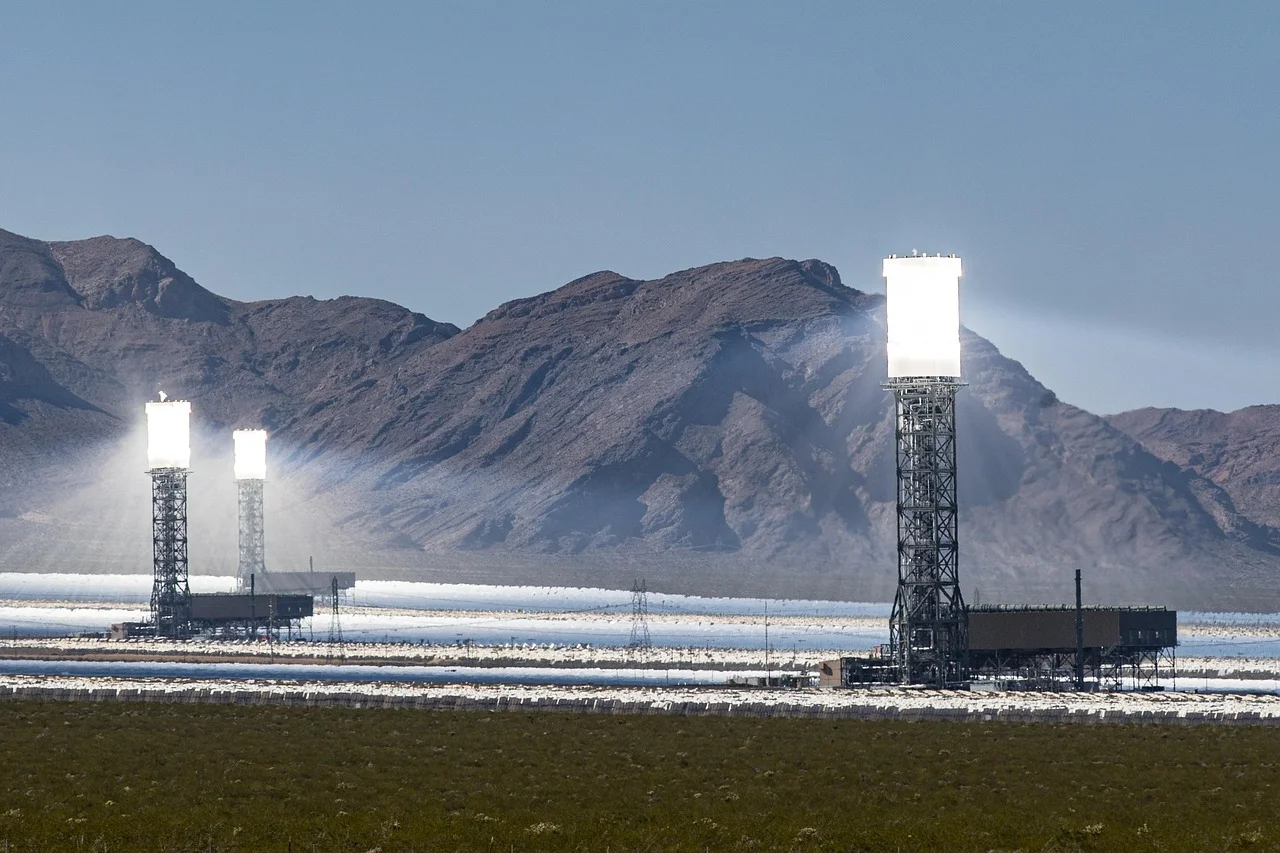 Tres torres solares con intensa reflexión de heliostatos en un valle desértico frente a montañas rocosas