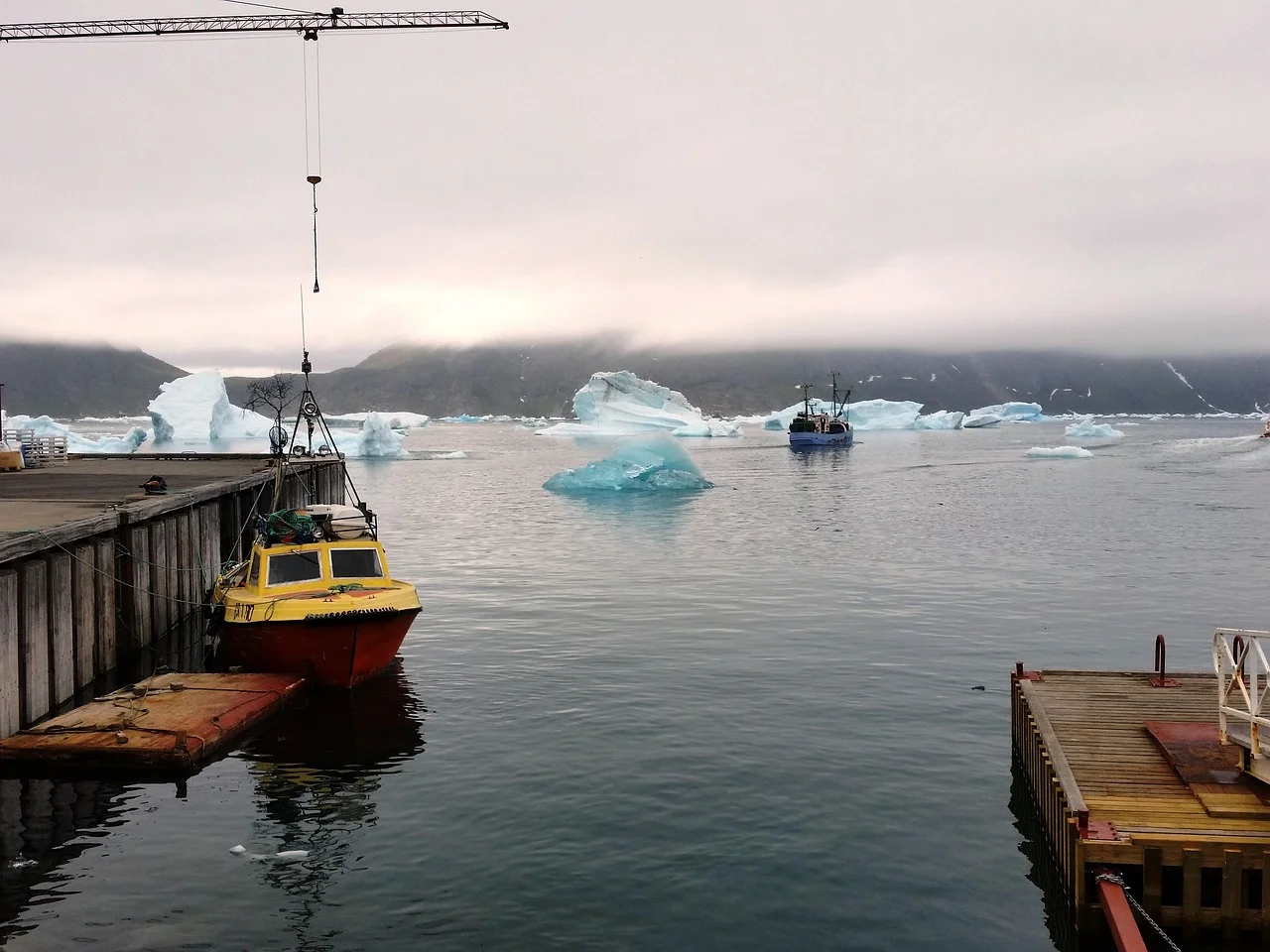 Botes en un muelle de Groenlandia con icebergs flotando en el fiordo