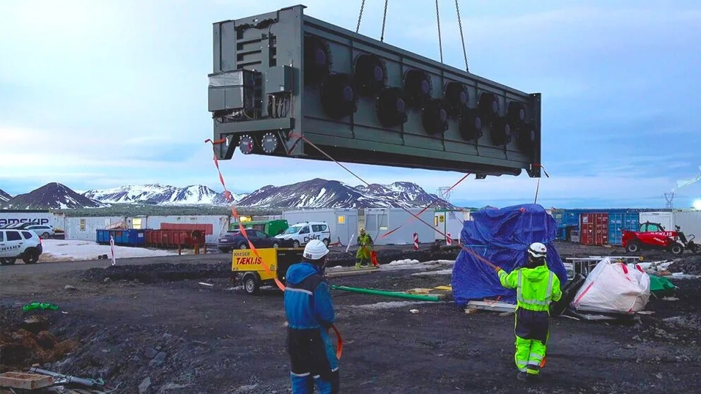 Trabajadores instalan un módulo de captura de carbono en la planta Orca, con montañas nevadas al fondo