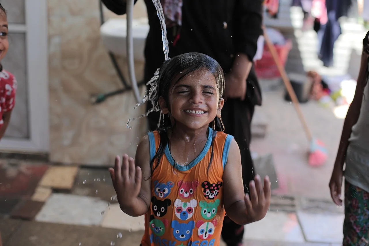 Niña riendo mientras se moja con agua en Gaza