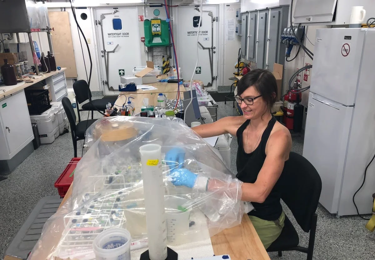 Investigadora trabaja en un laboratorio a bordo de un barco, manipulando muestras bajo una cubierta de plástico para evitar contaminación por oxígeno