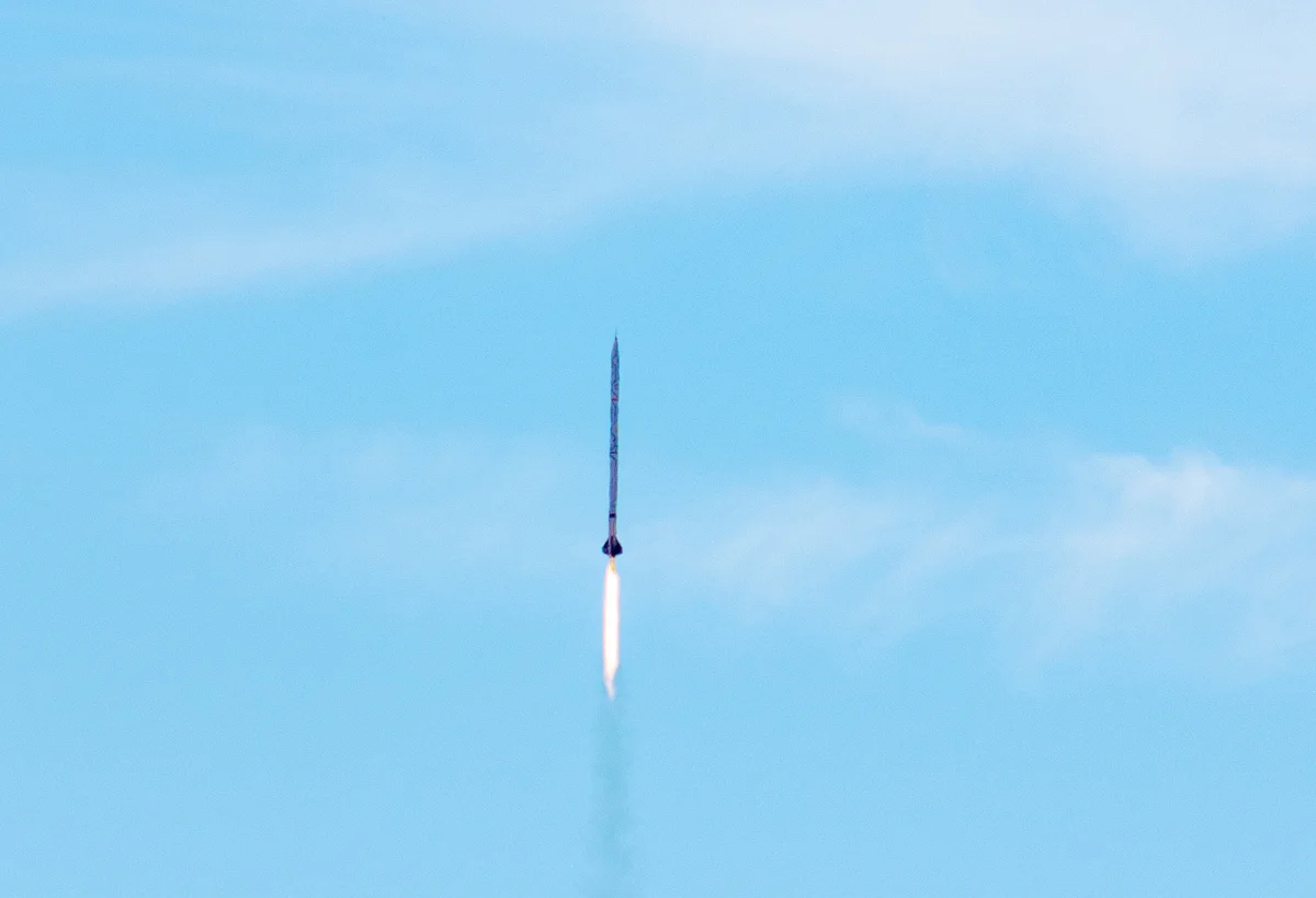 El cohete ISPIDA asciende dejando tras de sí una delgada estela blanca que contrasta con el cielo despejado.