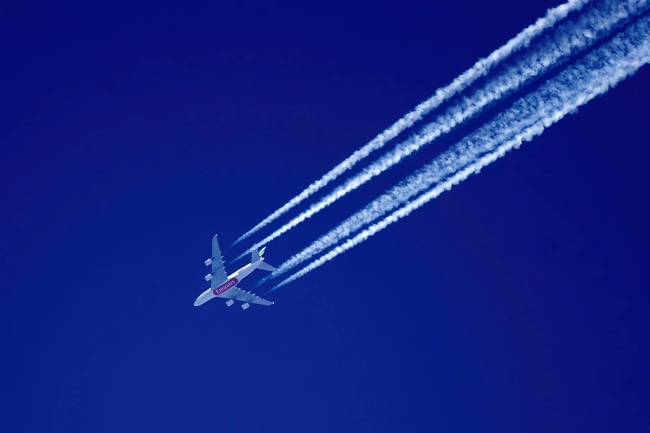 Avión comercial dejando estelas de condensación mientras vuela en un cielo azul despejado