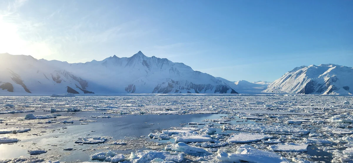 Hielo costero adherido a la costa con montañas y glaciares al fondo en la Antártida