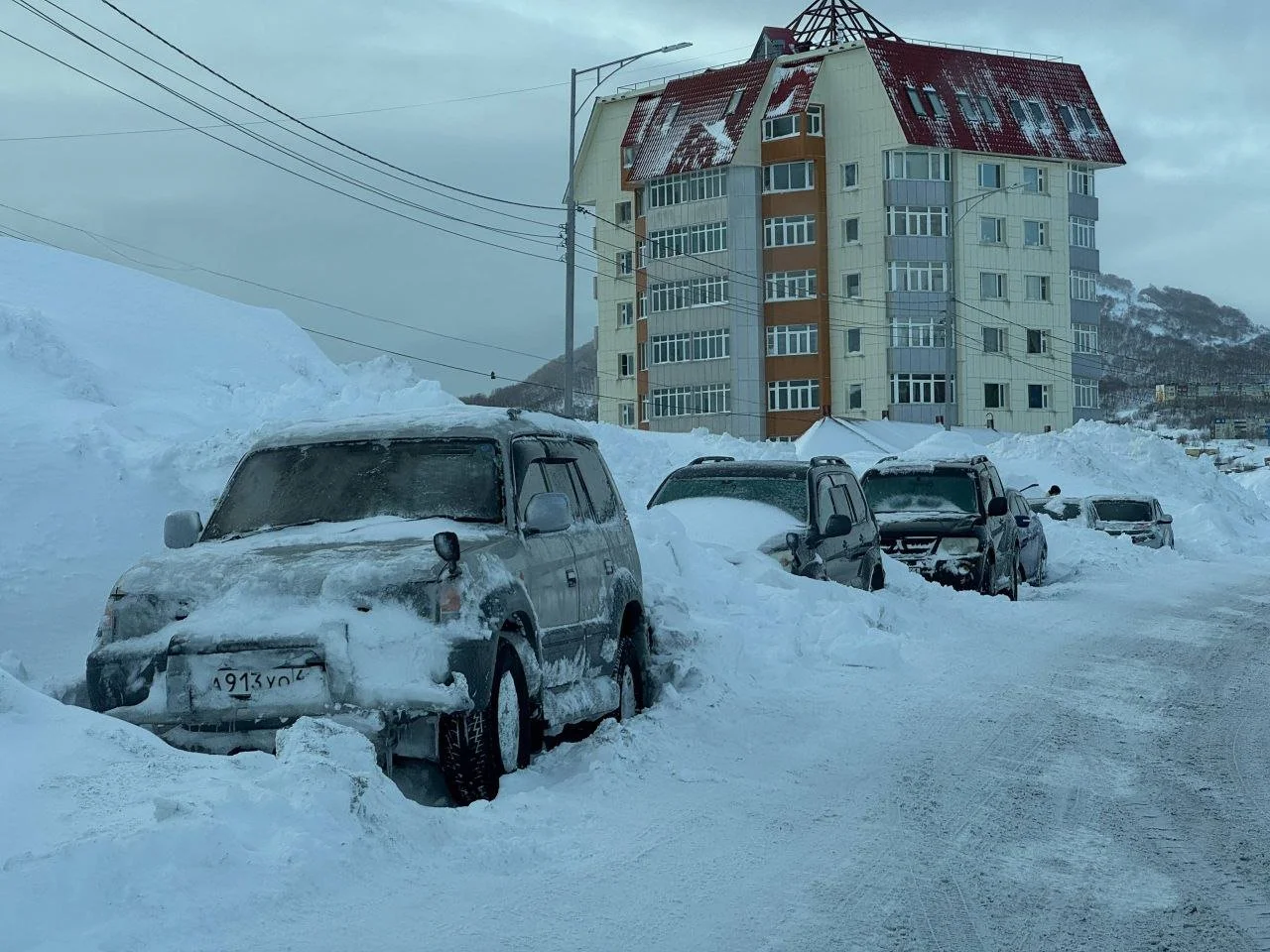 Calle urbana con coches y aceras casi sepultados por la nieve durante una tormenta