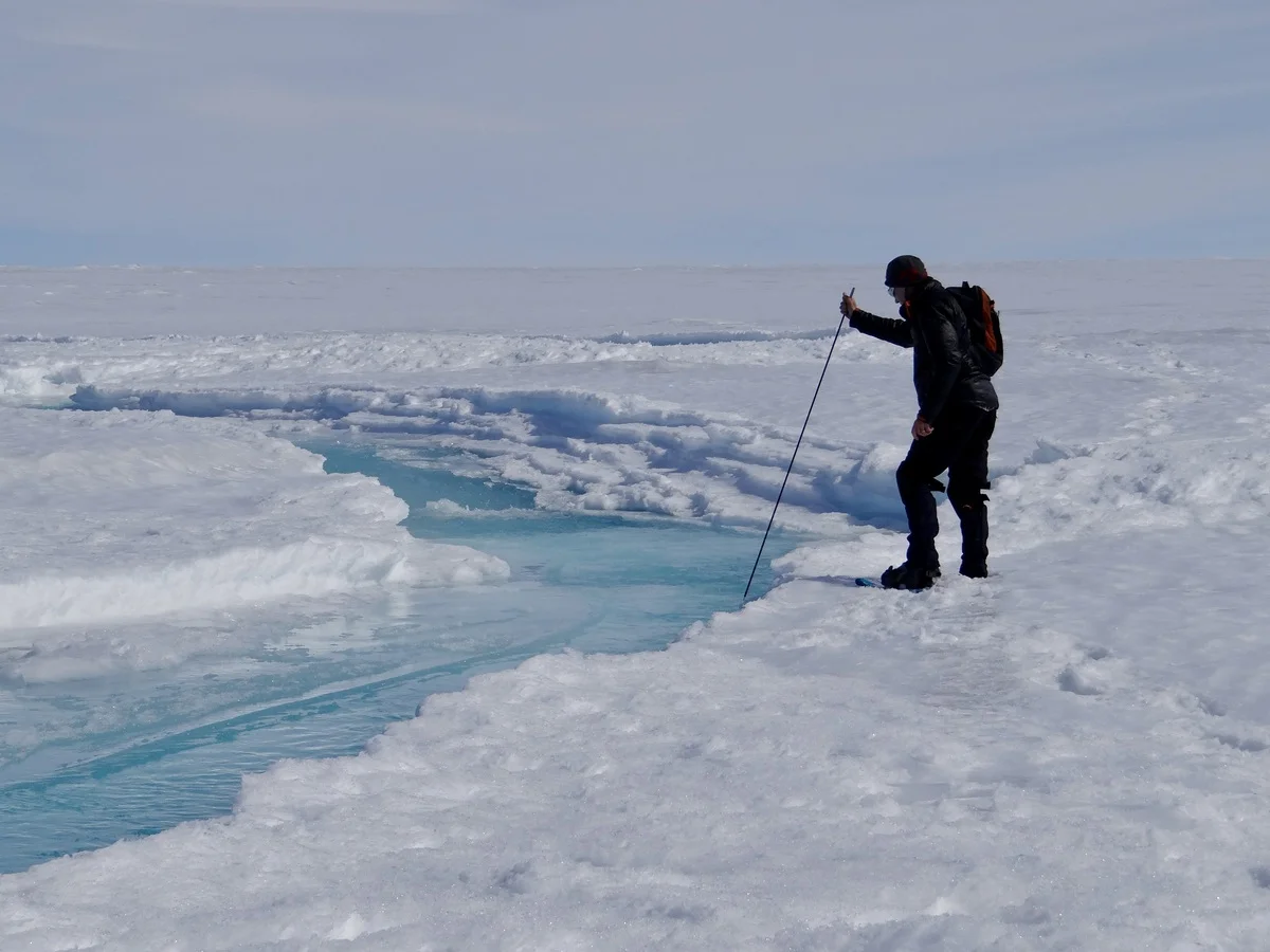 Investigador caminando sobre el hielo junto a un arroyo de deshielo