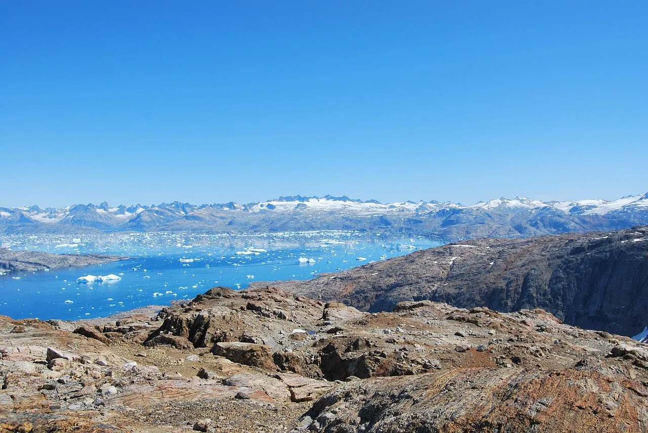 Paisaje de Groenlandia con montañas nevadas y témpanos flotando en el mar durante el deshielo