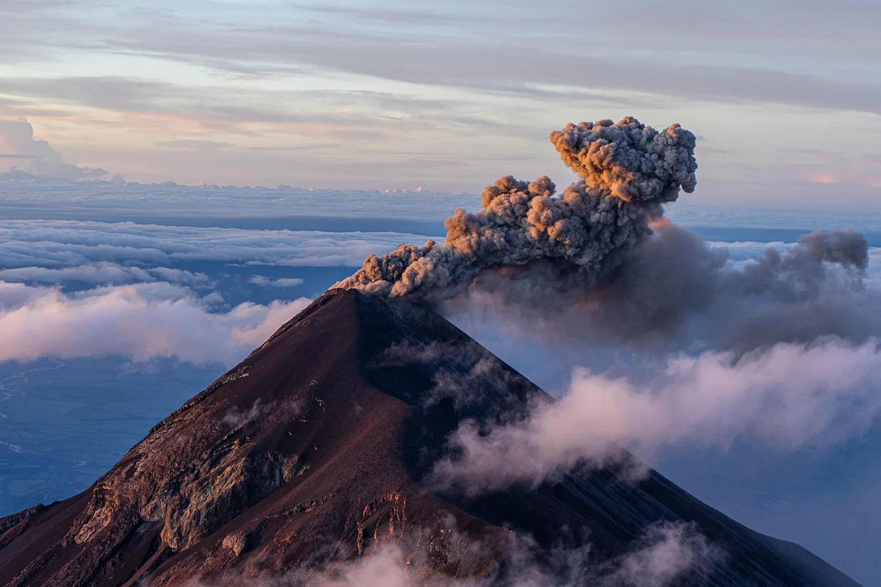 Volcán en erupción expulsando ceniza sobre las nubes al amanecer