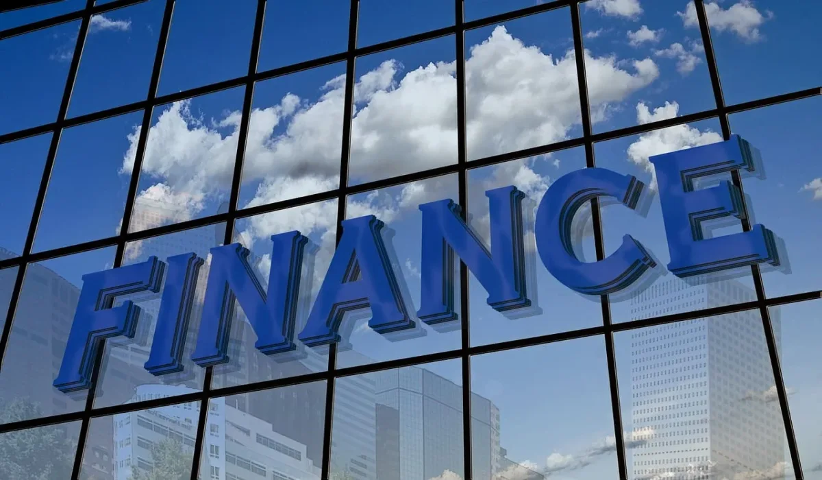 Fachada de un edificio con la palabra 'Finance' reflejada en los ventanales, junto a un cielo azul con nubes.
