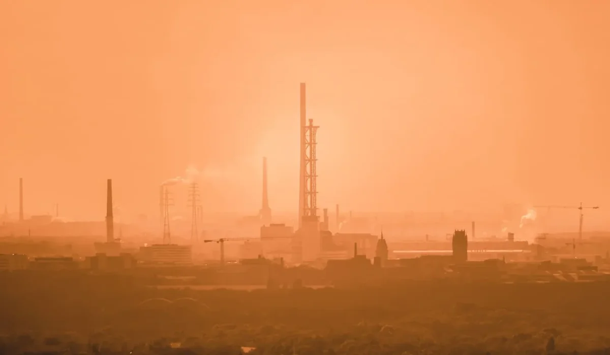 Vista de una ciudad bajo un denso manto de contaminación, destacando chimeneas y edificios industriales con un cielo naranja difuso.