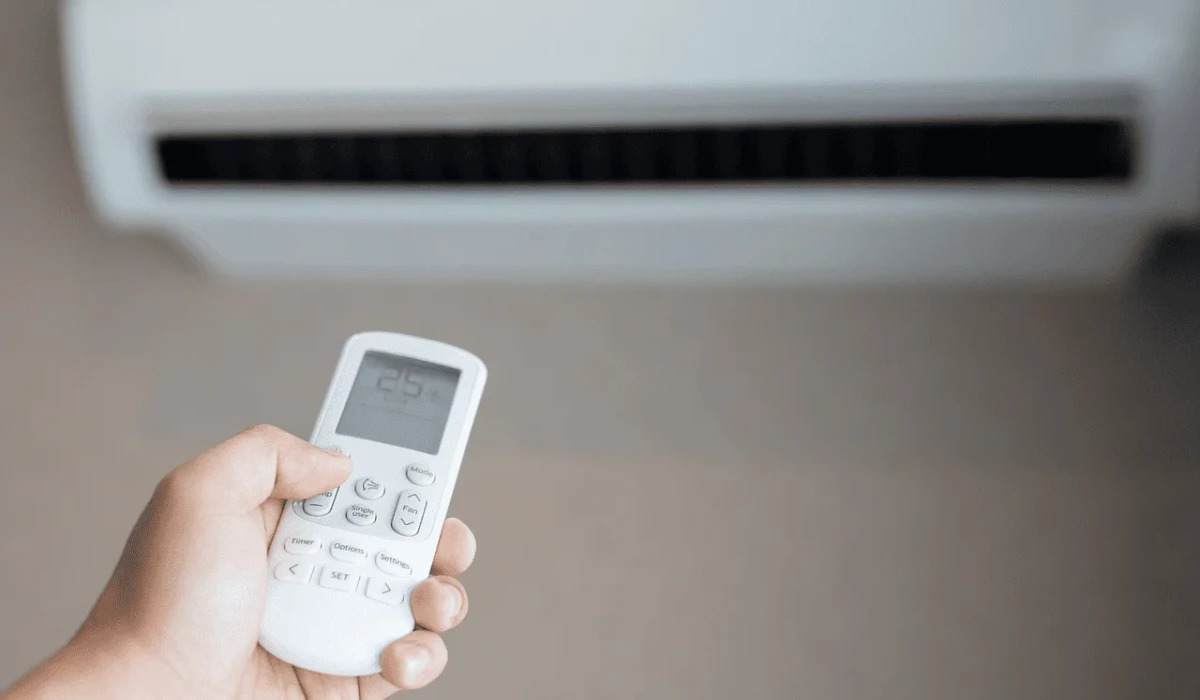 Control remoto apuntando hacia un aire acondicionado con pantalla digital que muestra la temperatura.