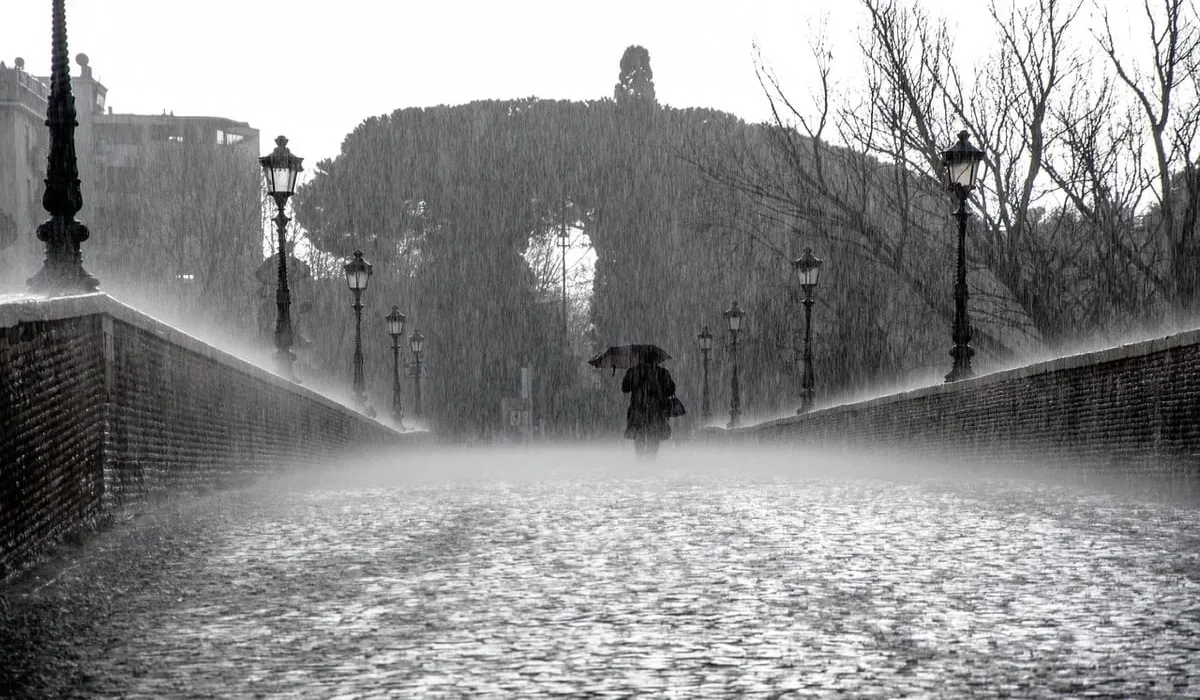 Persona caminando bajo la lluvia en un puente antiguo