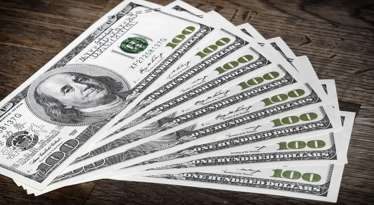 Fajo de billetes de 100 dólares estadounidenses extendidos sobre una superficie de madera.