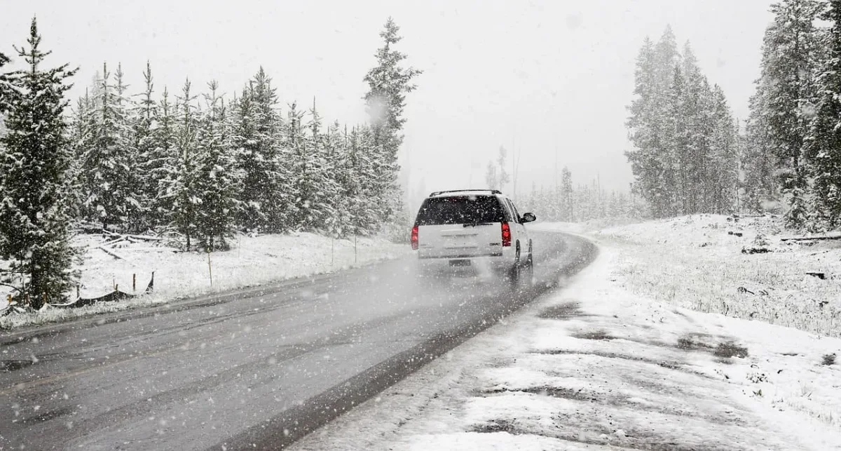 Vehículo circulando por una carretera nevada durante condiciones invernales, rodeado de árboles cubiertos de nieve.