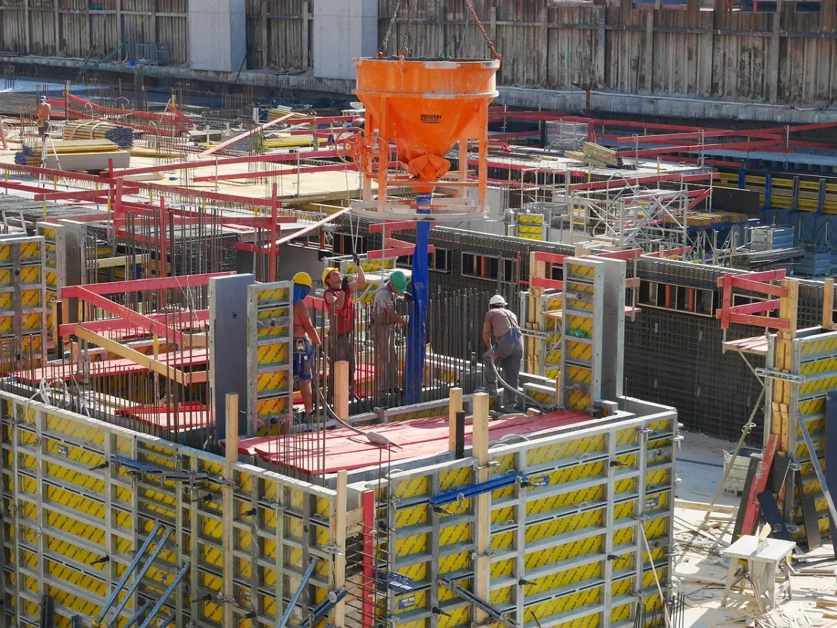 Obreros trabajando en la construcción de una estructura de concreto armado con encofrado y maquinaria, rodeados de andamios y materiales