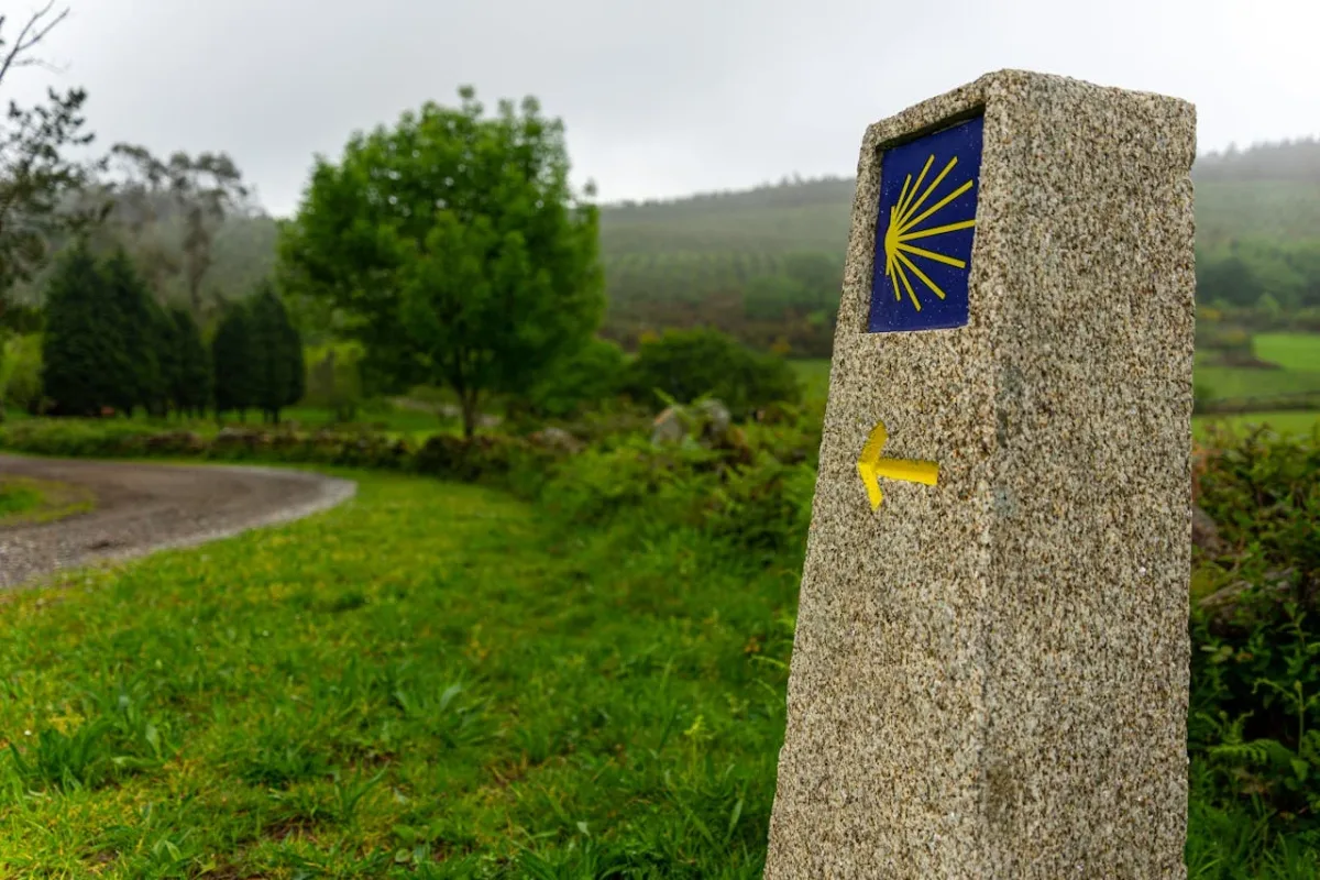 Mojón de granito con la concha amarilla, símbolo del Camino de Santiago, en un sendero rural de Galicia