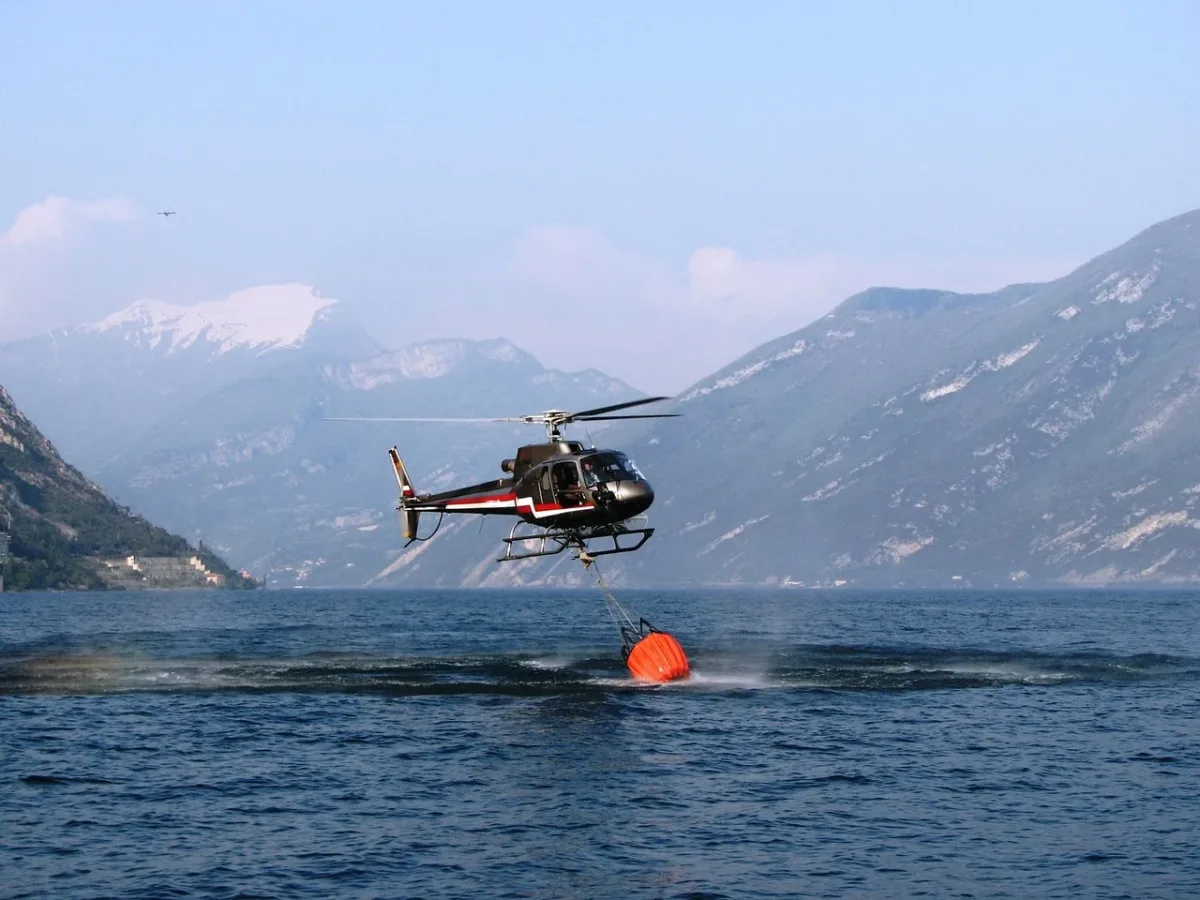 Helicóptero recogiendo agua de un lago con un helibalde para combatir incendios forestales