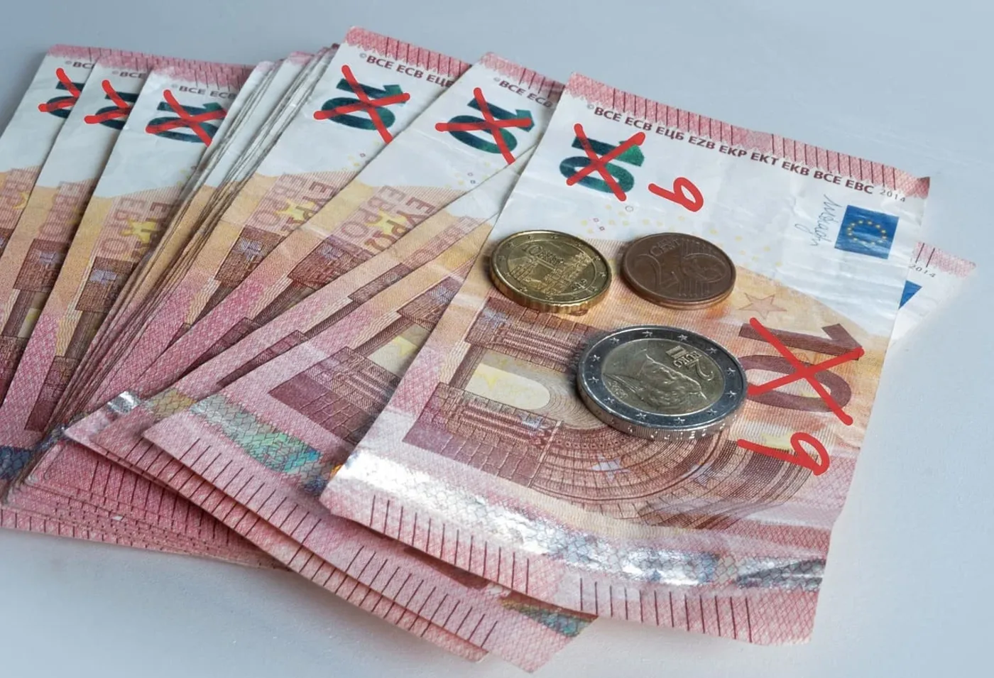 Billetes de euro marcados con cruces rojas y monedas apiladas, representando temas de inflación o desvalorización monetaria.