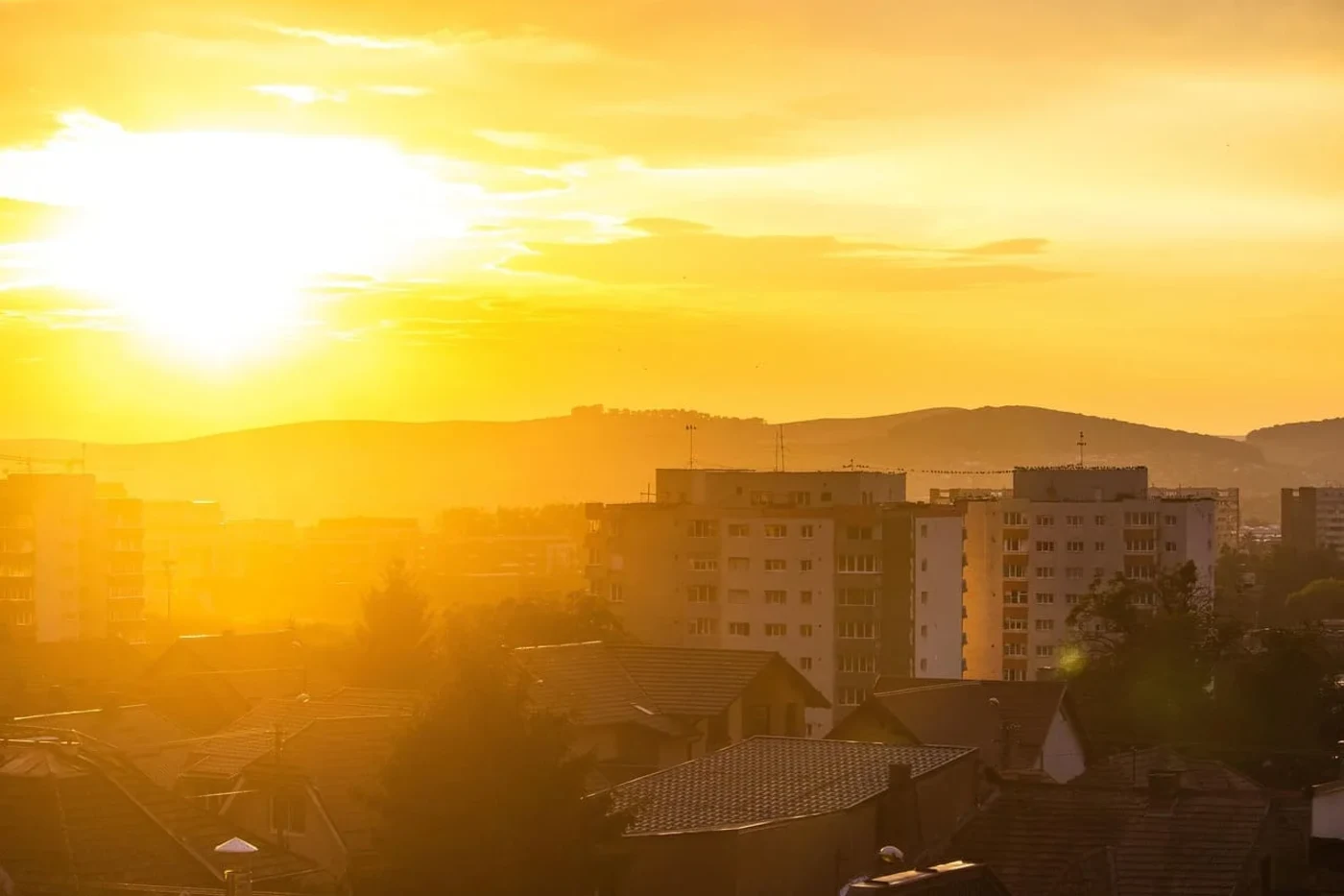 Atardecer dorado sobre una ciudad con edificios residenciales y colinas al fondo.