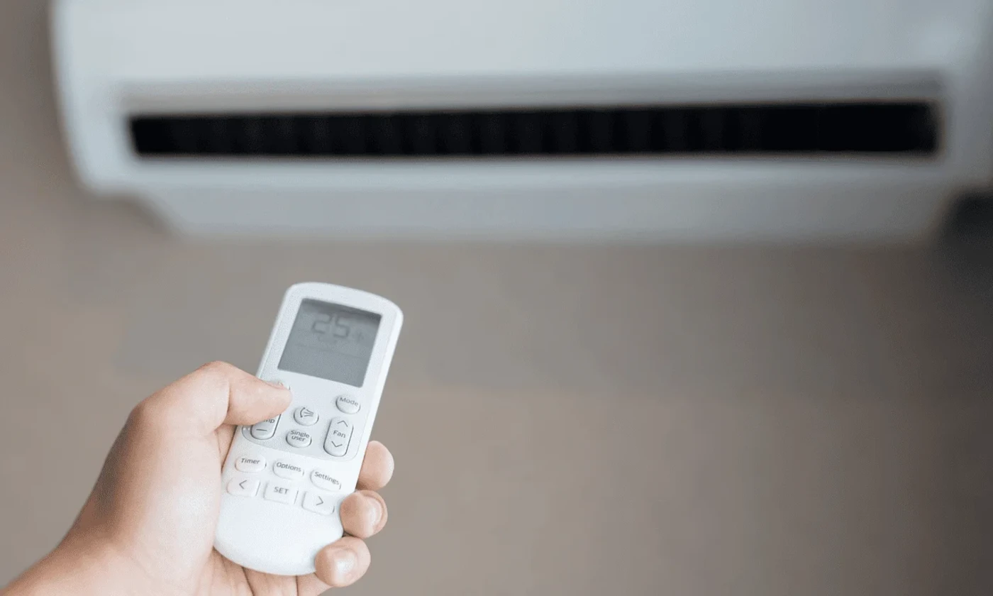 Control remoto apuntando hacia un aire acondicionado con pantalla digital que muestra la temperatura.
