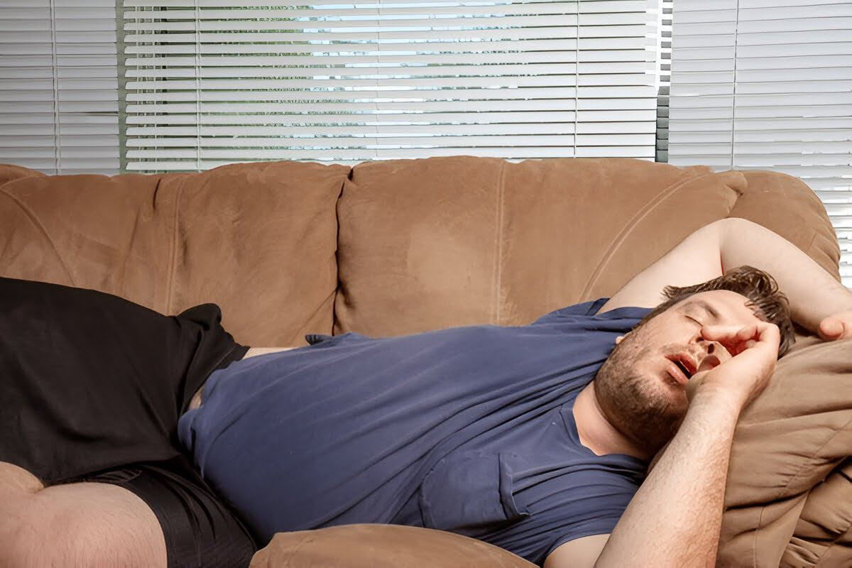An overwieght man sleeping on the couch in a weird position and snoring