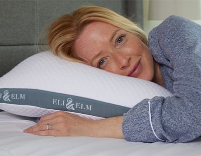 A woman resting her head on a white Eli & Elm cooling side sleeper pillow with her hand tucked under