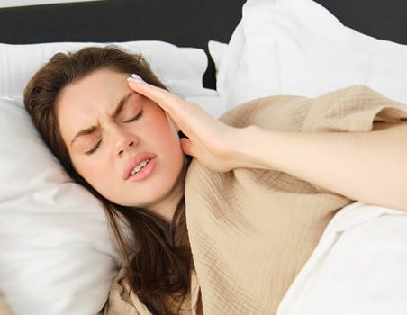 A women lying on bed putting hand over forehead showing she has headache.