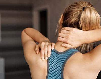 A woman with one hand over her shoulder and the other on the back of her neck, in pain