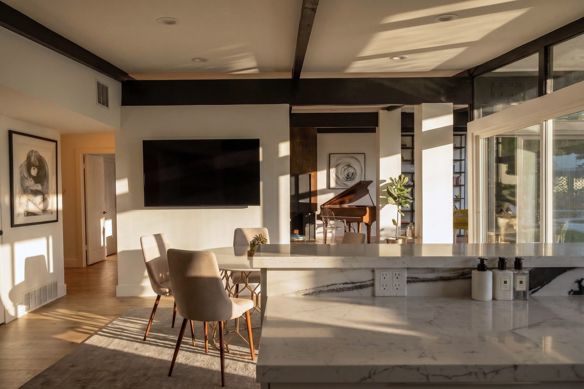 The living room with glass walls and exposed wood beams overhead, afternoon light filling the space.