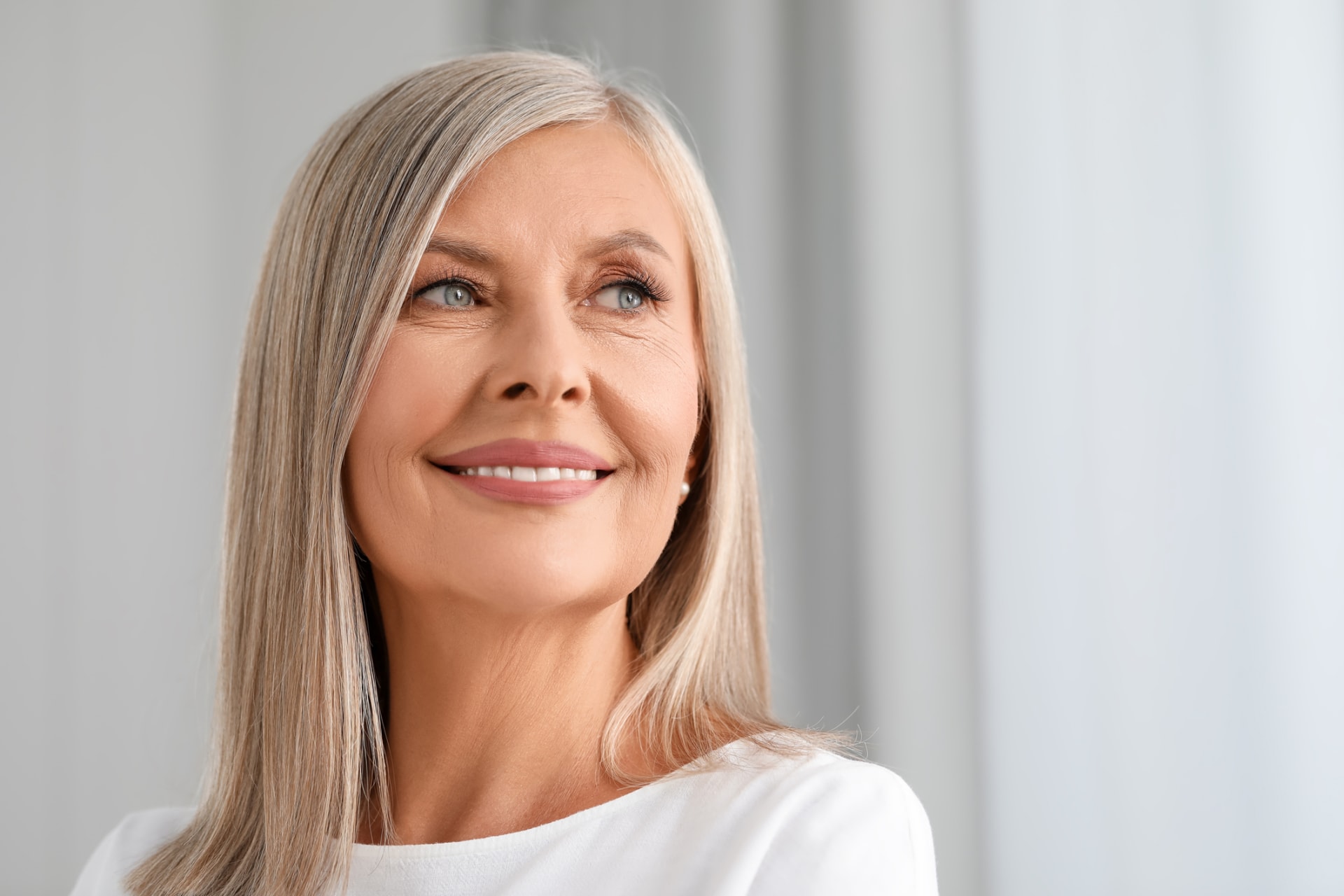 Mohs surgery: Smiling mature woman with long gray hair looking toward a window