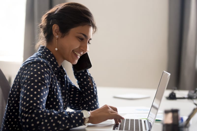 woman with pearl earrings and polka dot blouse talking on a cell phone in front of a laptop