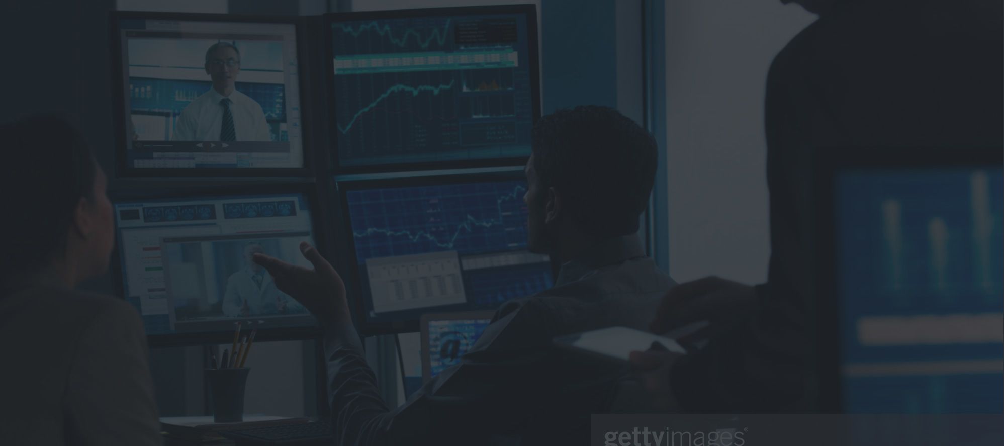 a man sitting in a chair pointing at several screens showing news and stock market graphs