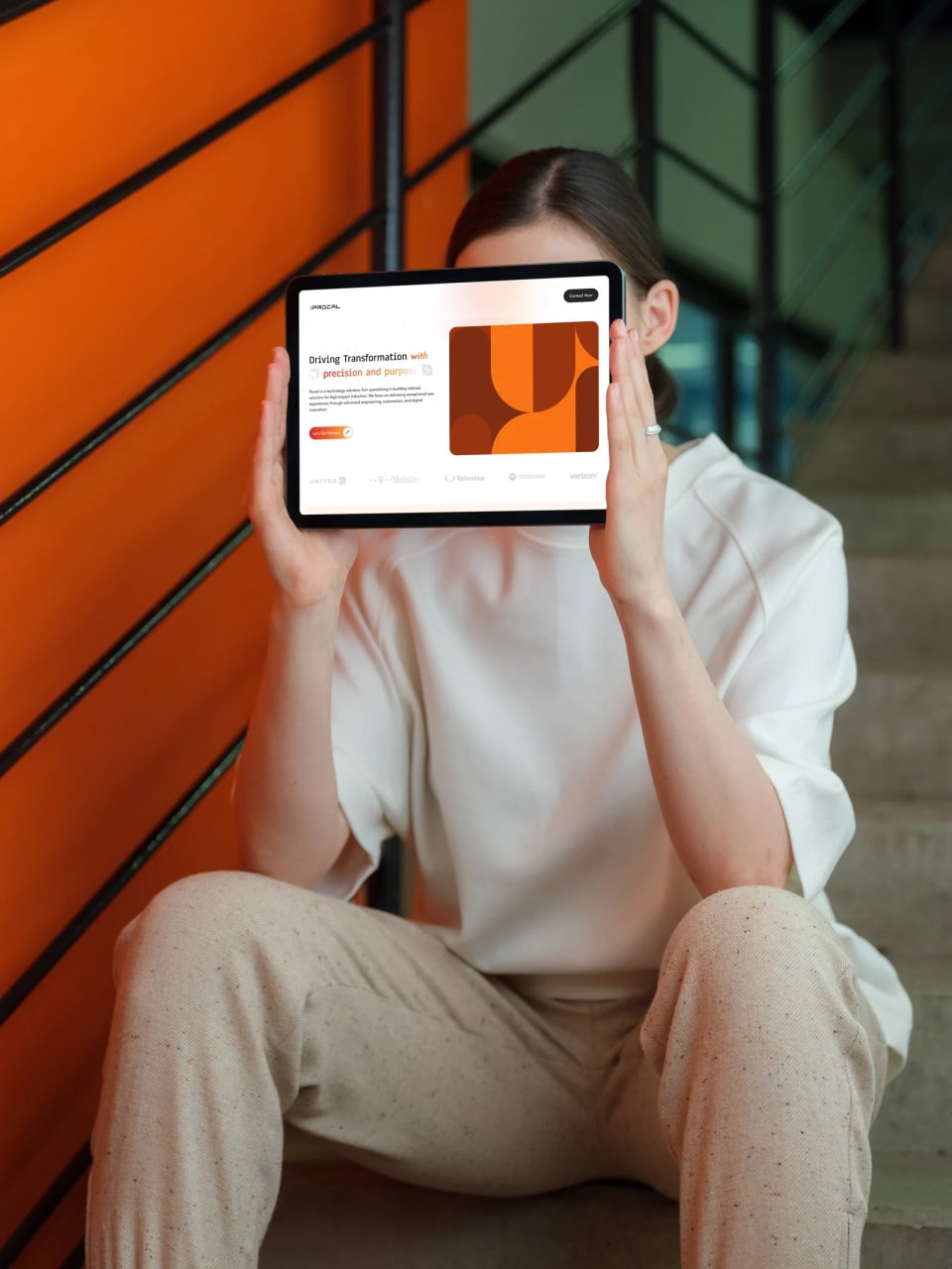 A seated person holding a tablet displaying Procal’s white and orange website