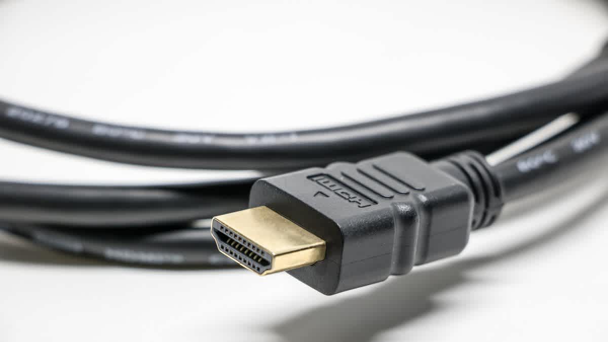Several HDMI cables laid out on a desk next to a games console and a gaming monitor