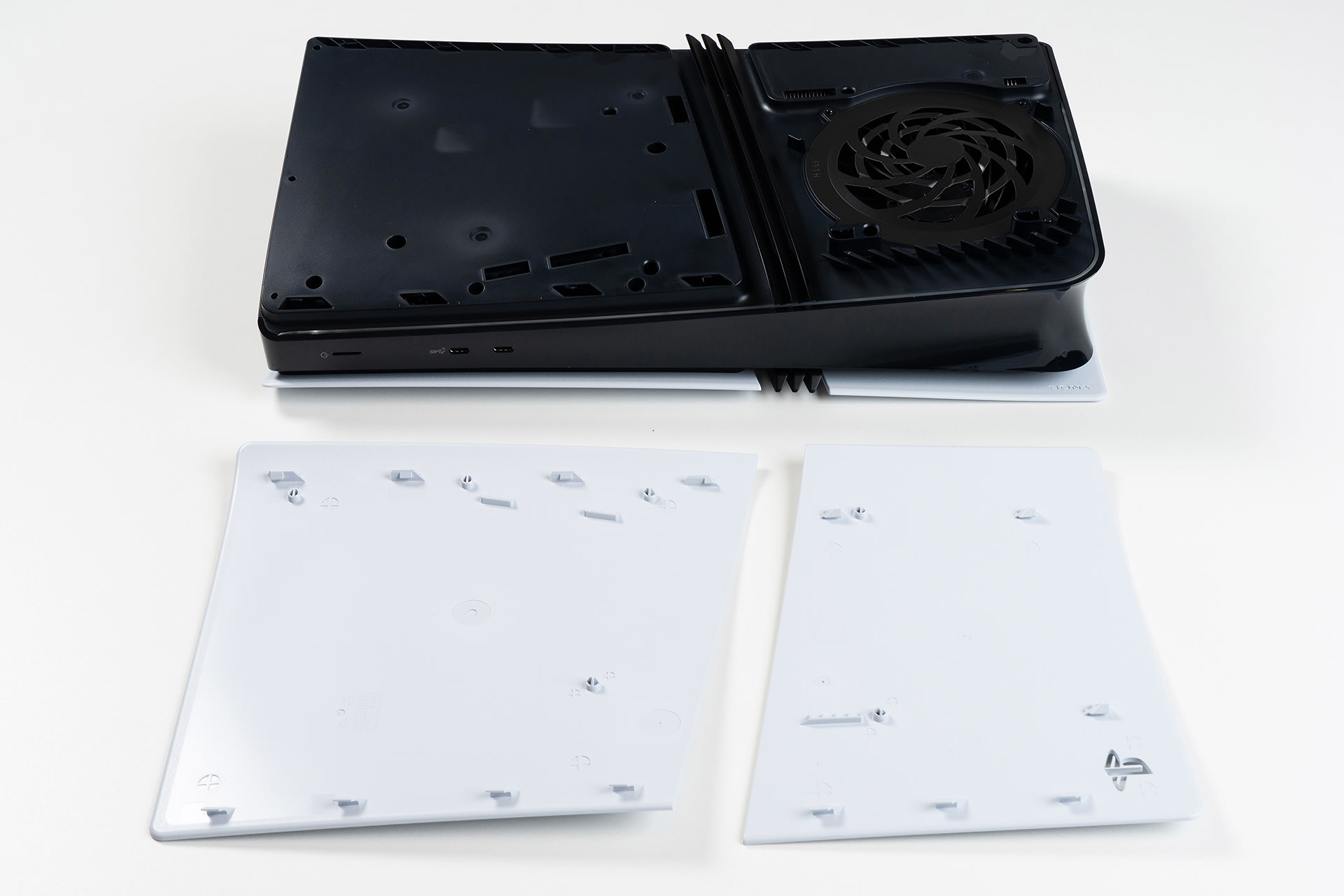 A PlayStation 5 with the side panel removed exposing the internal fan and drive bay