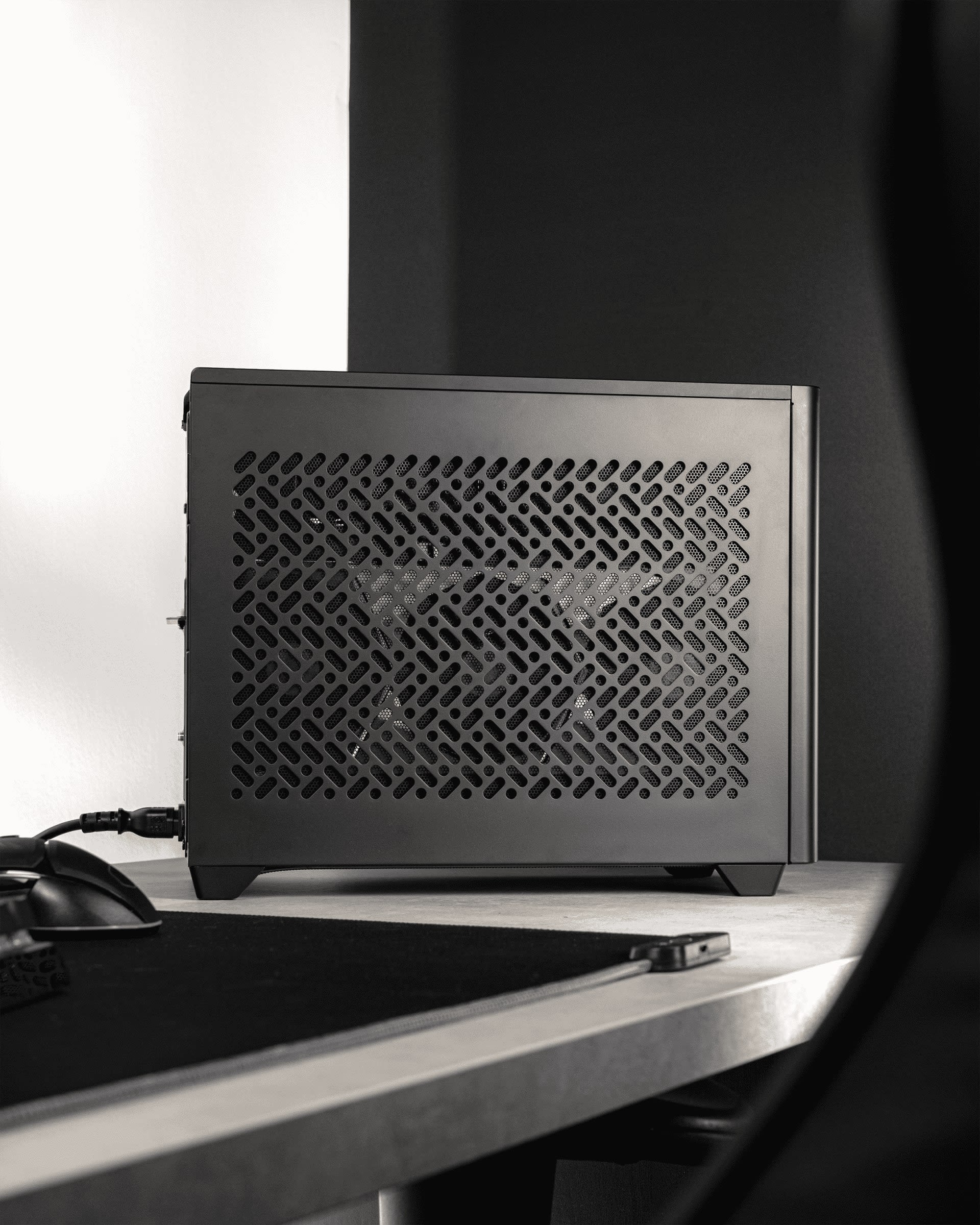 Black Cooler Master NR200P V2 small form factor case sitting on a desk beside a mouse and mouse mat
