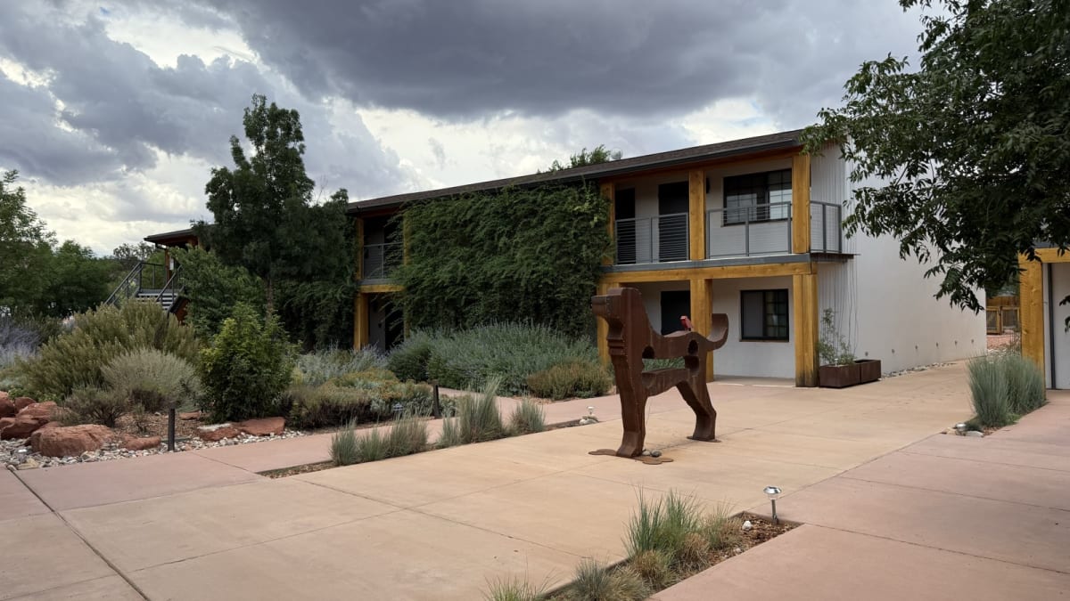 Two-story Best Friends Roadhouse building with wood-framed balconies, native desert landscaping, and a steel dog sculpture in the courtyard in Kanab, Utah