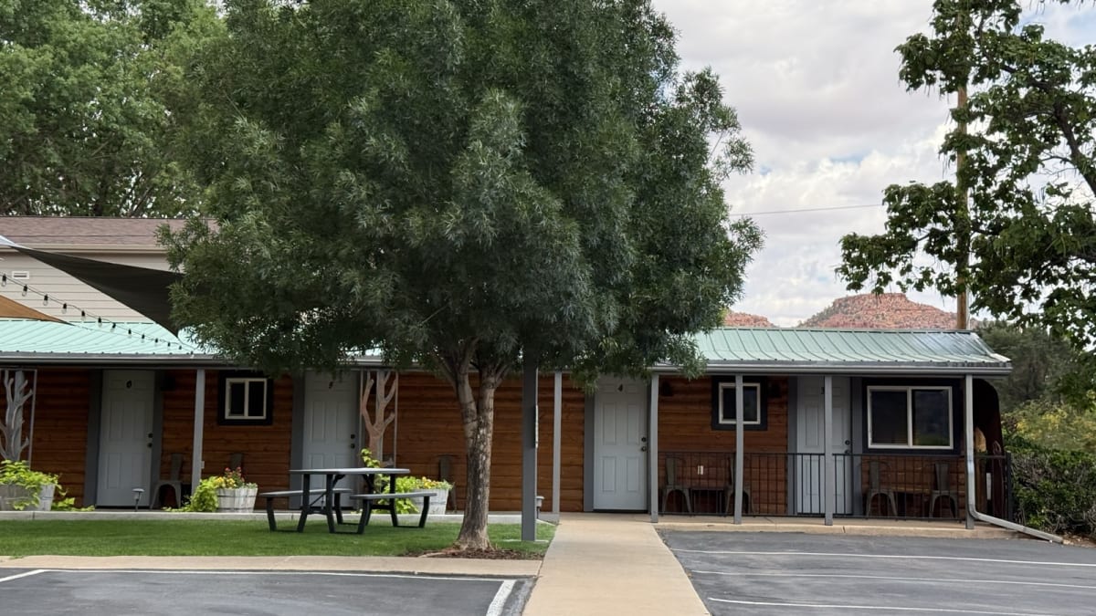Single-story log-cabin guest rooms at Canyons Lodge with green metal roofs, string lights, and red cliffs behind in Kanab, Utah
